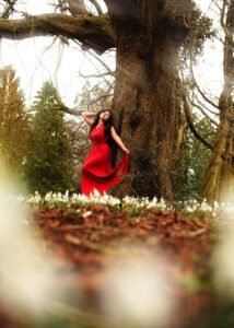Empowering Female Portrait Photography – A woman in a flowing red dress stands by a grand tree, exuding confidence and strength in an outdoor Nottingham photoshoot.