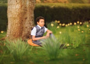 Portrait of a boy sitting under a tree during a family outdoor photoshoot in spring at Elvaston Castle Park, Derby.