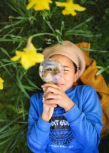 Nottingham Family Photographer - Professional family outdoor photoshoot in spring at Elvaston Castle Park, capturing a portrait with a magnifying glass amidst blooming daffodils