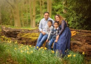 Family of four smiling and sitting on a log surrounded by daffodils during a spring family photography session