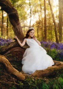Girl in white communion dress sitting on tree trunk during First Holy Communion Photography