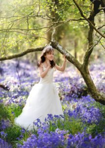 Girl posing under tree in bluebell field for First Holy Communion Photography in Nottingham