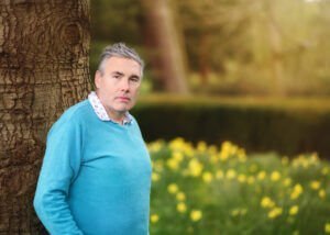 Nottingham Family Photographer - Portrait of a dad posing next to a tree with blooming daffodils in the background, taken at Elvaston Castle Park during a professional family outdoor photoshoot in spring.