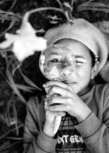 Nottingham Family Photographer - Portrait of a boy surrounded by blooming daffodils, holding a magnifying glass during a spring family outdoor photoshoot at Elvaston Castle
