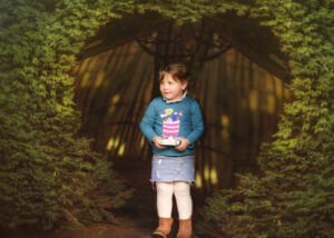 Portrait of a girl holding a camera with a heart-shaped hedge background during a professional family outdoor photoshoot in spring at Elvaston Castle Park, Derby.