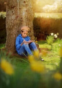 Portrait of a boy writing in his diary under a blooming daffodil tree during a family photoshoot at Elvaston Castle Park, captured by Nottingham Family Photographer.