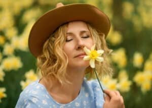 Soft & Feminine Female Portrait Photography – A close-up of a woman in a blue dress, eyes closed, savoring the scent of a flower, celebrating beauty and presence.