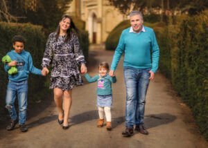 Family of 4 walking hand in hand, smiling, with Elvaston Castle in the background during a professional outdoor photoshoot in spring.