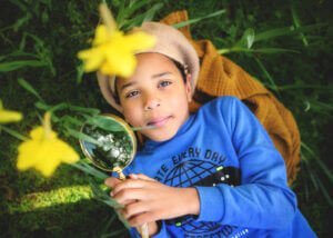 Portrait of a boy holding a magnifying glass during a professional family outdoor photoshoot at Elvaston Castle Park in Derby in spring. Captured by Nottingham Family Photographer