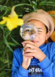 Portrait of a boy holding a magnifying glass at Elvaston Castle Park during a professional family outdoor photoshoot in spring. Captured by Nottingham Family Photographer.