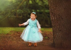 Cheerful toddler girl playing hide and seek at Elvaston Castle Park during a family outdoor photoshoot in spring by Nottingham Family Photographer