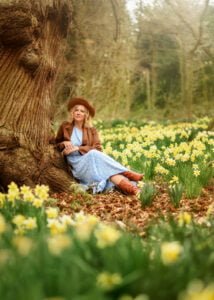 Outdoor Female Portrait Photography – A woman in a light blue dress leans against a tree, surrounded by daffodils, capturing peace and self-love in Nottingham.