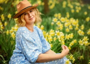 Radiant Female Portrait Photography – A smiling woman in a blue dress sits among daffodils, embracing joy and natural beauty in Nottingham.