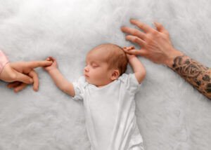 Newborn baby peacefully sleeping, holding her parents' hands during a heartwarming Newborn Lifestyle Photoshoot by Nottingham Family Photographer