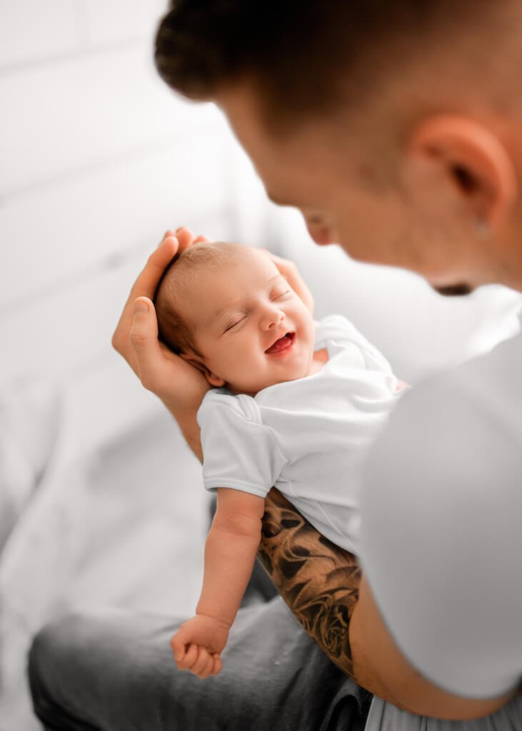 Smiling newborn baby cradled in dad's hands during a Newborn Lifestyle Photoshoot.