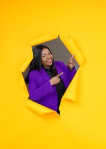 A businesswoman is wearing a violet suit on a yellow background during a branding photoshoot for a business coach's website.