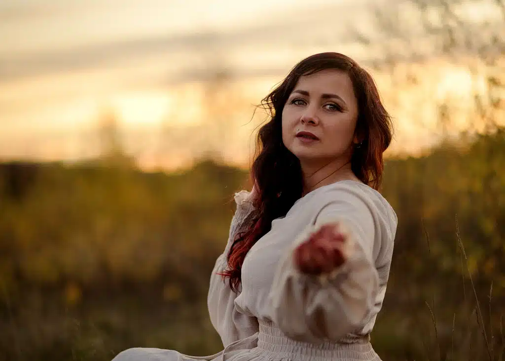 A mature woman in a light dress reaching out with a serene expression during sunset in Nottingham.