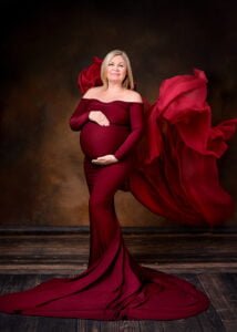 Pregnant woman in burgundy maternity photoshoot dress with flying fabric in studio