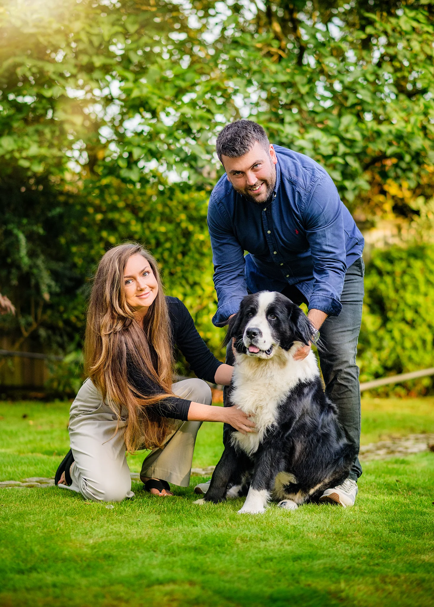 Happy couple kneeling and hugging their fluffy dog during a family garden photoshoot in Nottingham