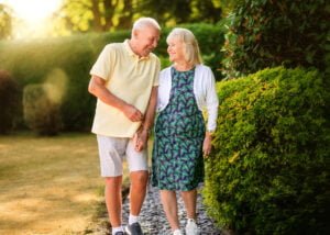 An elder couple walking hand in hand, sharing a tender moment in their lush garden at sunset