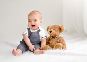 Adorable baby sitting with a teddy bear in a studio photoshoot by a professional family photographer.