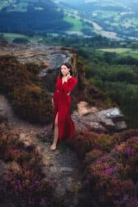 Confident woman in a striking red dress stands amidst the heather at Mother Cap, her gaze inviting a connection.