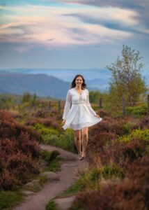 Joyful woman in a white dress walking along a path at Mother Cap, surrounded by heather, embodying freedom and grace.