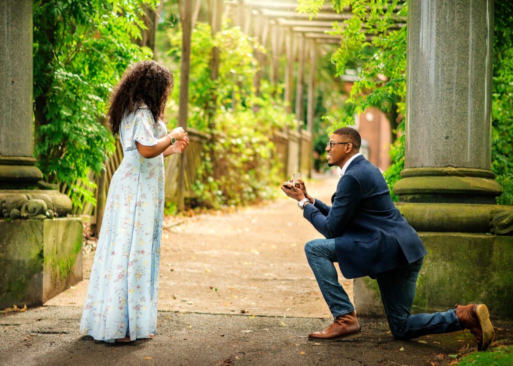 Surprised woman being proposed to by a man on one knee in a serene Nottingham garden, encapsulating the essence of engagement photography.
