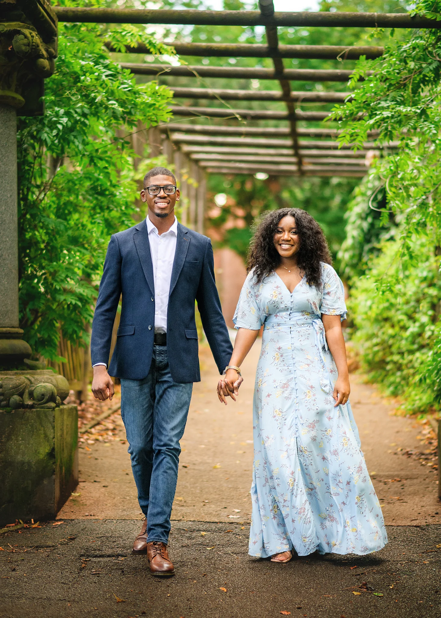 Happy couple holding hands and walking through a vine-covered archway, embodying engagement joy in Nottingham