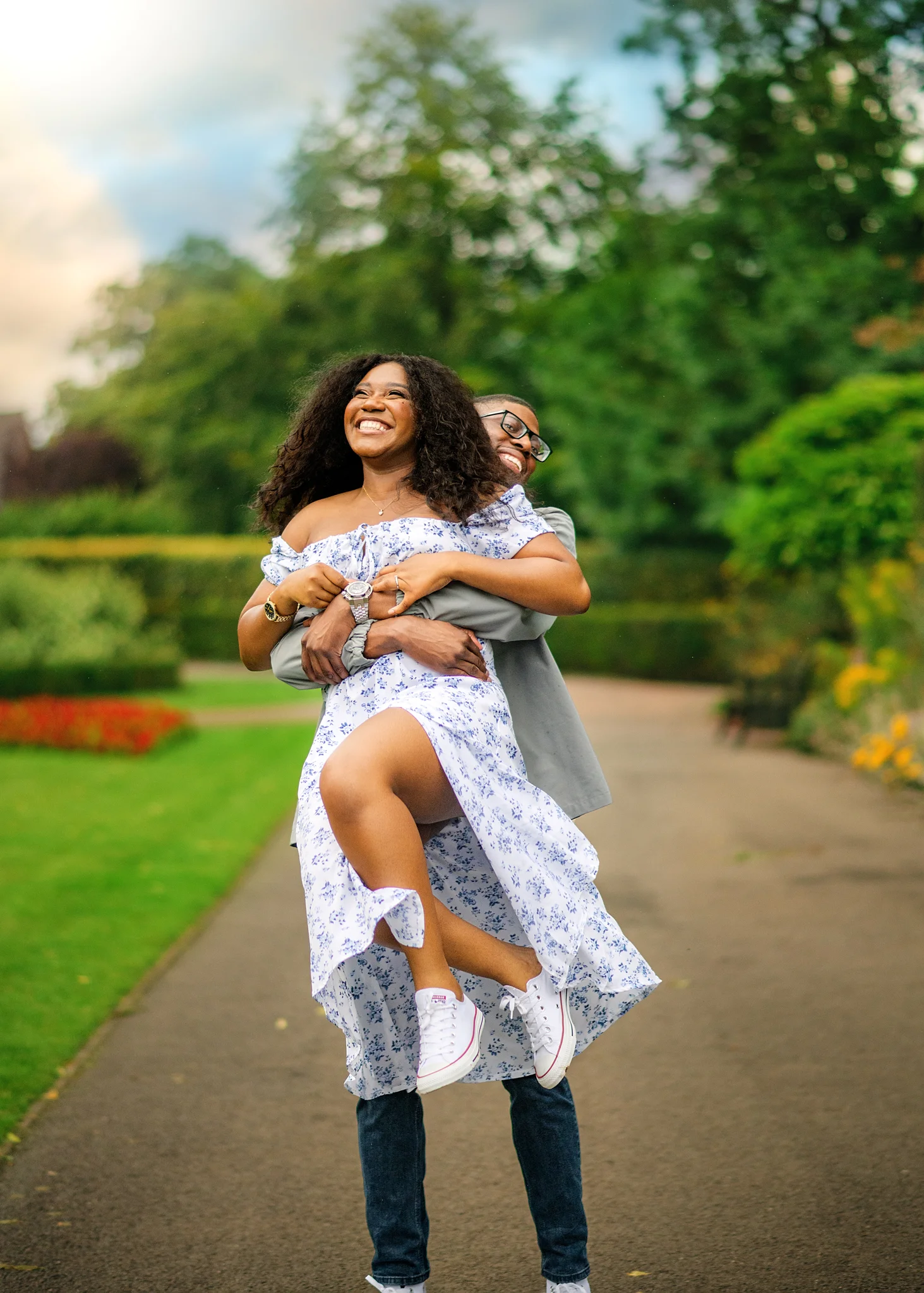 Man carrying his laughing fiancée in a garden, their engagement joy evident in their bright smiles