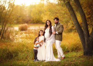 A beautiful family portrait in an autumnal setting, with the expectant mother in a white lace gown, lovingly surrounded by her daughter, son, and partner.