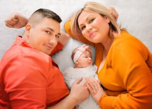 Newborn sleeping peacefully between parents dressed in vibrant colors, their faces radiating happiness in a lifestyle newborn photography setting.