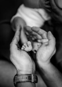 Black and white image of a newborn's tiny feet cradled in a parent's hands, showcasing the delicate nature of life in lifestyle newborn photography.