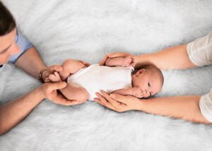 Newborn baby cradled securely by mother's and father's hands on a fluffy white background, gazing curiously in a lifestyle newborn photograph.