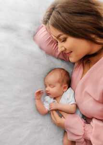Mother adoringly watches over her sleeping newborn, a tender moment of maternal love captured in a lifestyle newborn photography session.