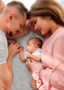 Parents lovingly gaze at their peaceful newborn, creating a family triangle of affection in a heartwarming lifestyle newborn photography moment.