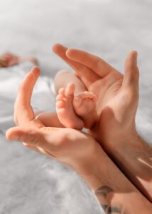 A father’s hands gently cradle his newborn’s tiny feet, a symbol of nurturing care in a lifestyle newborn photography image.
