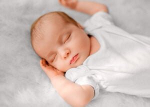 Serene newborn baby sleeping with a soft smile on a fluffy blanket, captured in a natural light lifestyle newborn photography session.