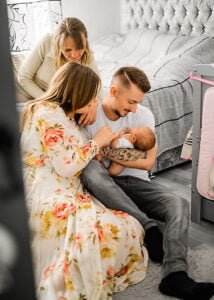 The multigenerational family moment with a grandmother, parents, and newborn baby in a cosy, lifestyle newborn photography session at home.