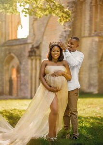 Expectant father placing a crown on his partner’s head as she poses in a golden gown during their maternity photoshoot in Nottingham.