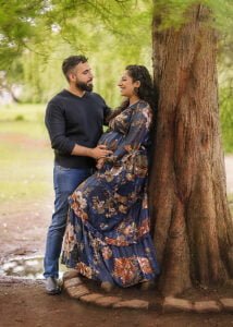 Couple leaning against a tree, sharing a loving moment during their maternity photoshoot in a serene park.