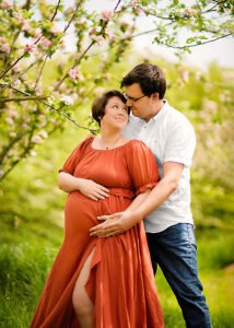 Loving couple in a maternity photoshoot among the blooming trees of Nottingham, sharing a tender, joy-filled moment.