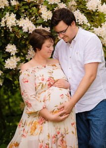 Expectant couple sharing a quiet moment in a spring orchard, sitting under a blossoming tree during their maternity photoshoot in Nottingham.