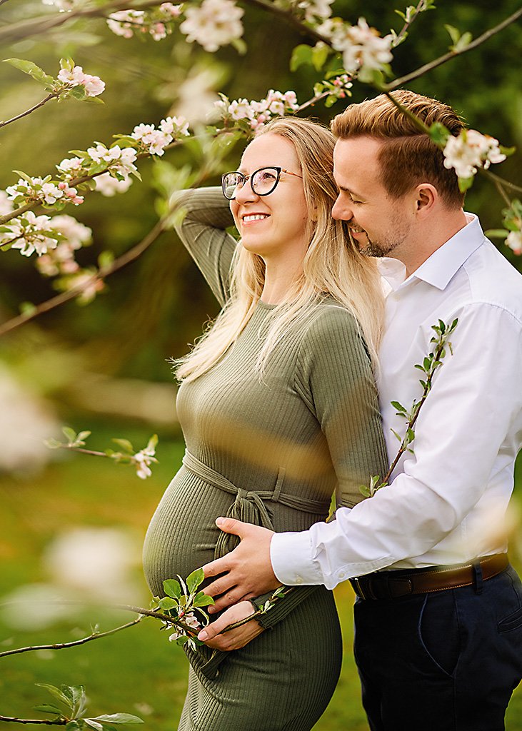 A blissful couple in a Nottingham spring maternity photoshoot, with the expecting father lovingly embracing the mother and her baby bump.