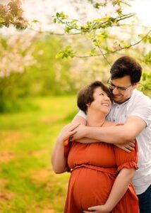 A couple sharing a tender moment in an orchard during a spring maternity photoshoot in Nottingham.