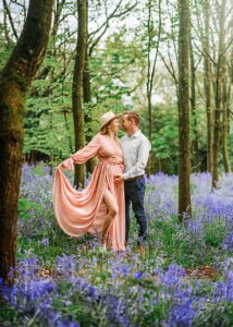 A couple posing in a blooming bluebell forest during their maternity photoshoot in Nottingham, with the mother-to-be wearing a flowing peach gown.