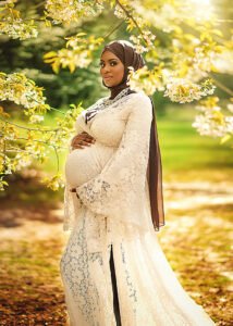 A radiant pregnant woman in a lace gown stands amidst the golden light of spring, her contentment shining through in a Nottingham maternity photoshoot.