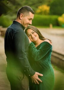 An expectant couple shares an intimate embrace, with the mother in a green velvet gown, symbolizing the vitality and love in outdoor maternity photography.