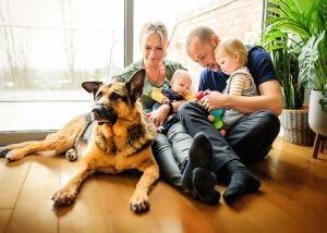 Joyful family with two children and a loyal German Shepherd dog enjoying a playful moment on the living room floor, encapsulating the essence of lifestyle newborn photography.