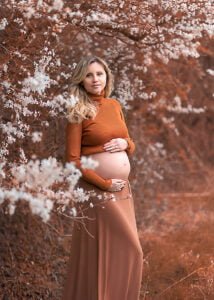 Pregnant woman in an autumn-inspired outfit posing against flowering branches during a maternity photoshoot in Nottingham.